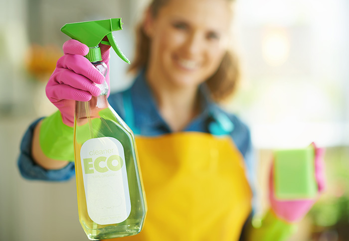 Woman showing spray bottle of eco friendly cleaning supplies at home